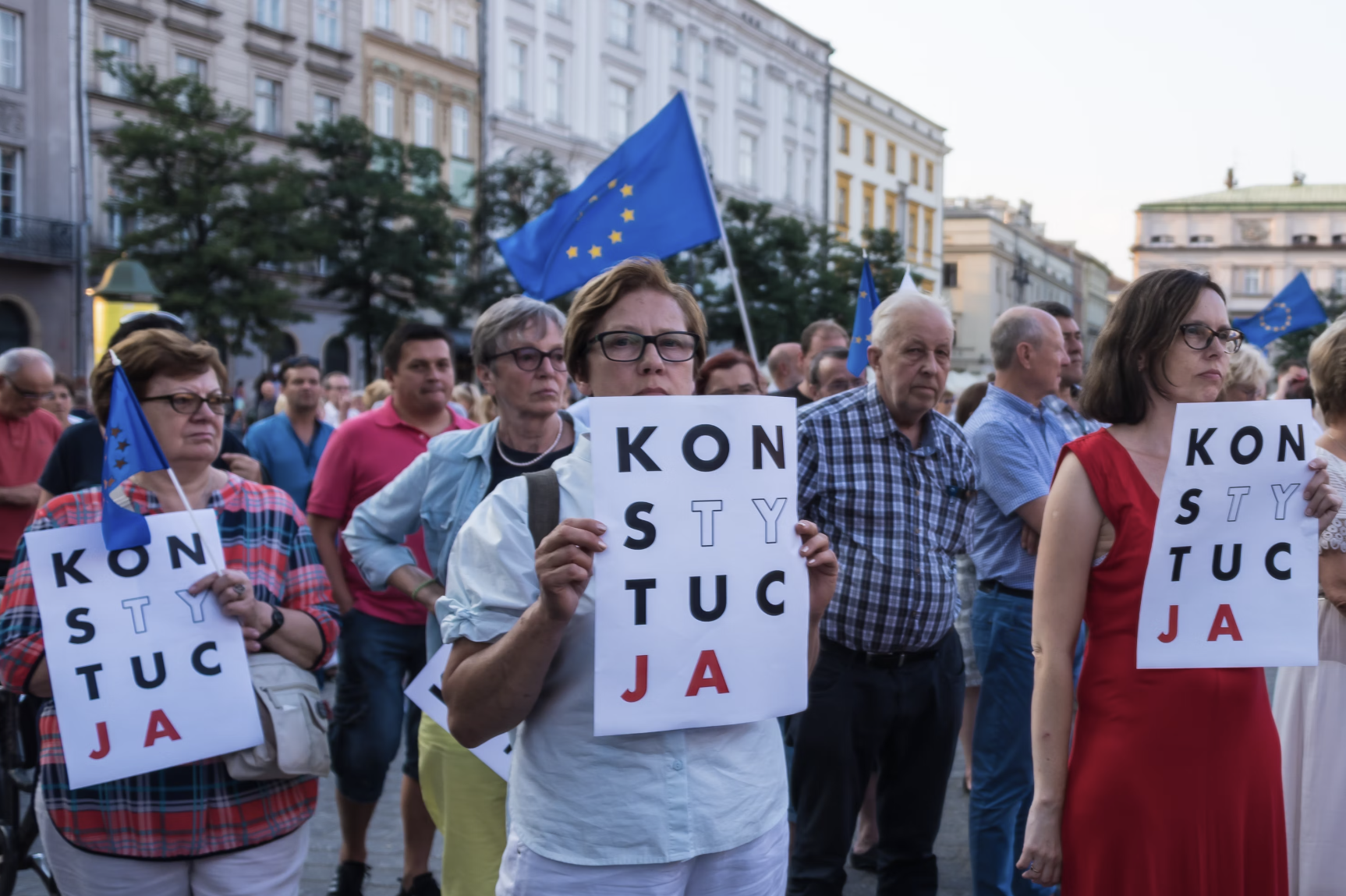 Protestors in Poland wave up European Union flags and hold signs with the Polish word for constitution.